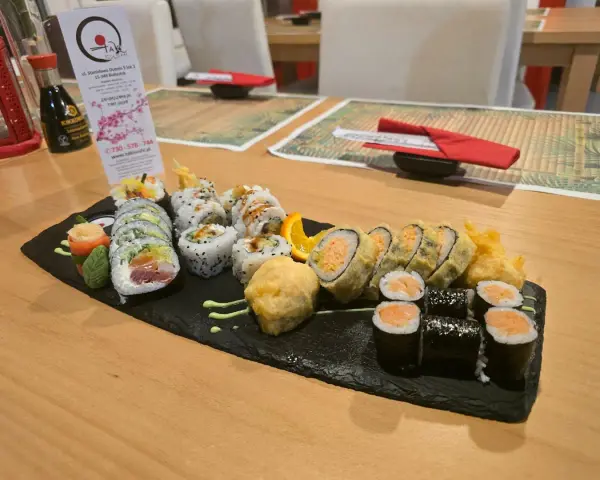 Talerz sushi z różnymi rolkami, w tym smażonymi i z łososiem, na czarnej desce.