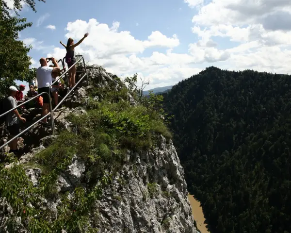 Grupa turystów na skalistym szczycie z widokiem na Pieniny i Dunajec.