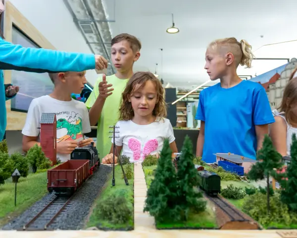 Dzieci oglądają makietę kolejową z pociągami i budynkami.