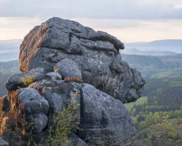 Skaliste formacje w Górach Stołowych z widokiem na zielone wzgórza i lasy.