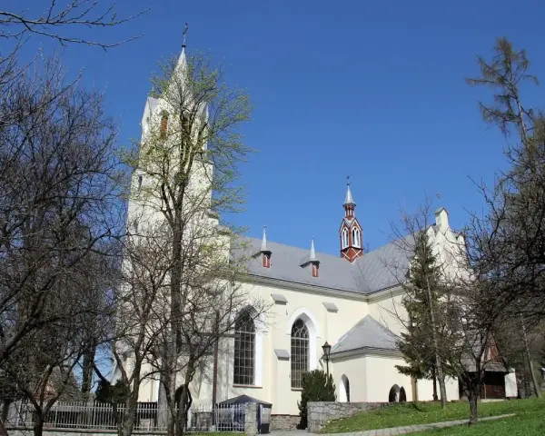 Jasny kościół św. Wojciecha w Szczawnicy z wieżą, otoczony drzewami.