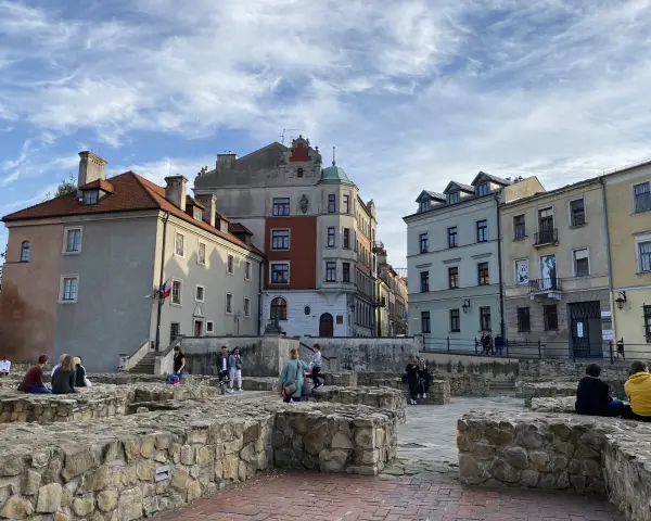 Ruiny zamku w Lublinie z ludźmi odpoczywającymi na kamiennych murach i zabytkowymi kamienicami w tle.