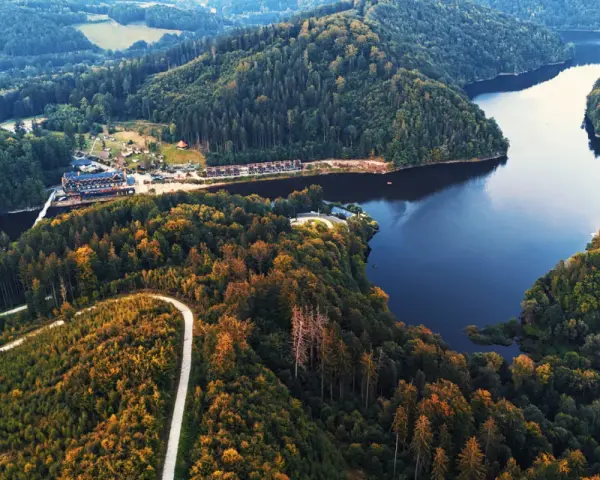 Widok z lotu ptaka na jezioro Bystrzyckie otoczone lasami, z krętą drogą i zabudowaniami.