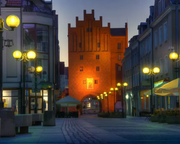 Brama miejska w Olsztynie o zmierzchu, oświetlona latarniami i iluminacją.