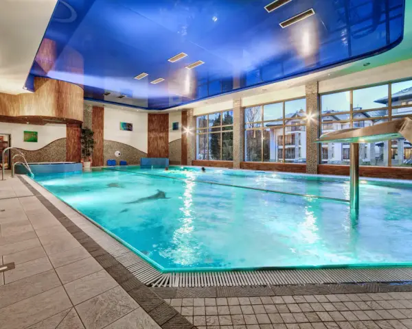 Basen hotelowy z niebieskim sufitem i dużymi oknami, woda w basenie jest turkusowa.