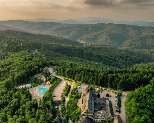 Widok z lotu ptaka na hotel SPA z basenem i zjeżdżalnią, otoczony lasem i górami.