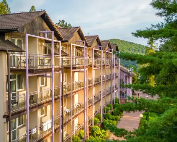 Hotel z balkonami w otoczeniu zieleni i gór.