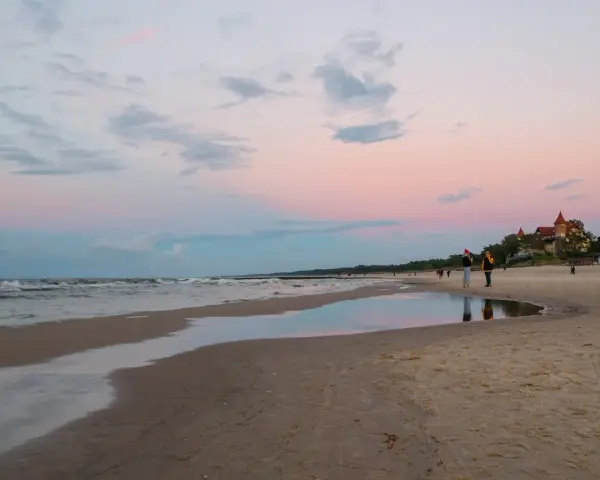 Plaża w Łebie o zachodzie słońca z widokiem na morze i budynek z czerwonym dachem.