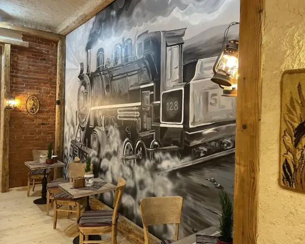 Wnętrze restauracji z muralem przedstawiającym lokomotywę i stoliki.