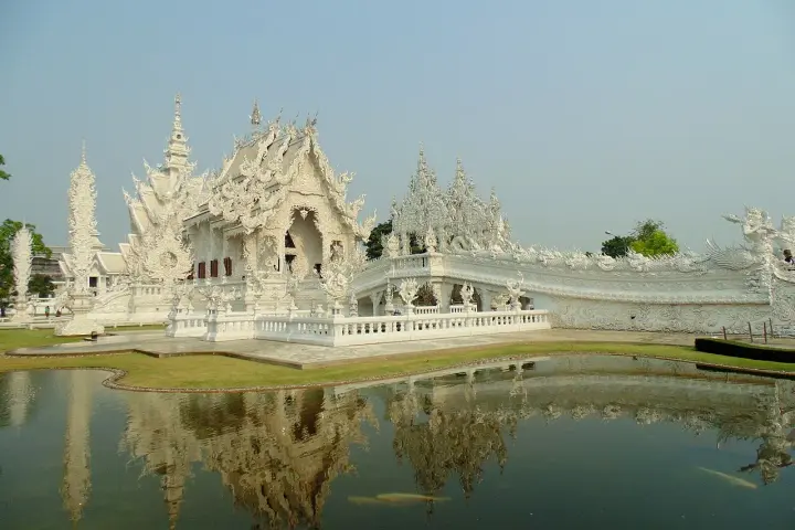 Biała świątynia Wat Rong Khun w Tajlandii z odbiciem w stawie.