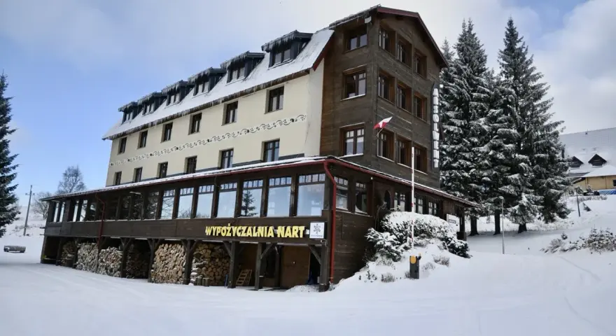 Hotel w Zieleńcu zimą, z widoczną wypożyczalnią nart i stosem drewna.