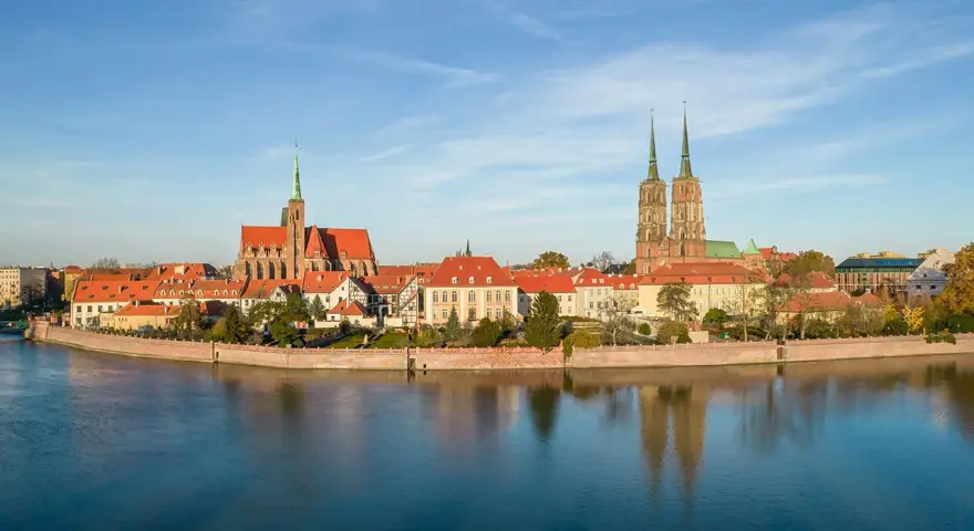 Widok na Ostrów Tumski we Wrocławiu z rzeką i odbiciem budynków w wodzie.
