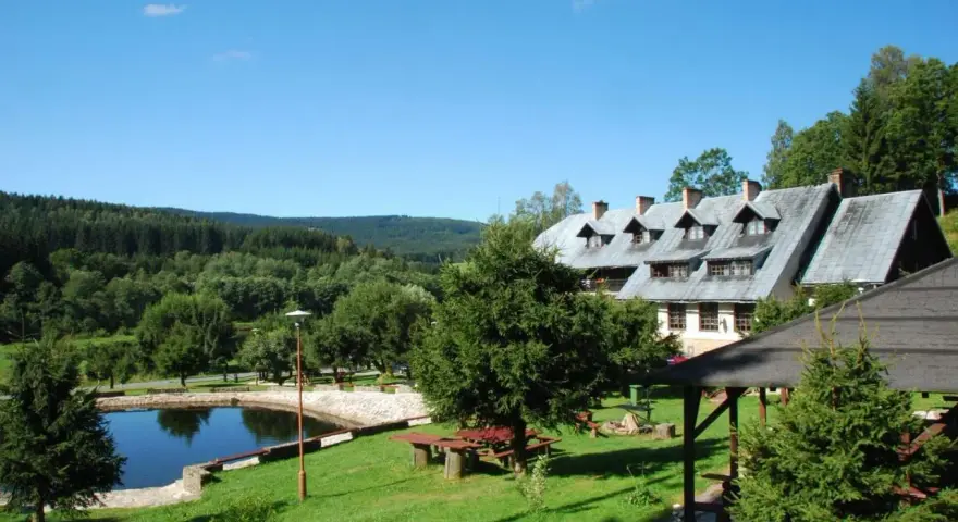 Budynek pensjonatu z kamiennym stawem i zielonym ogrodem w Górach Orlickich.