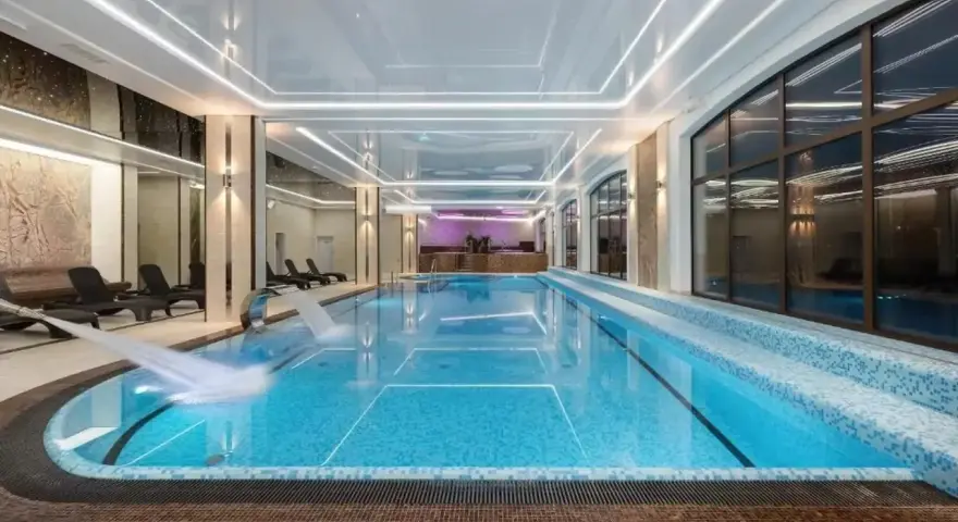 Nowoczesny basen w hotelu spa z wodospadem i leżakami.