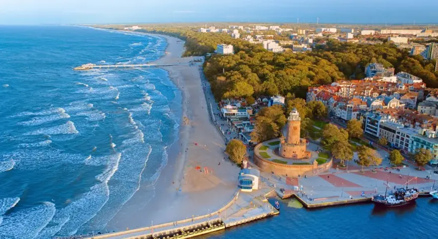 Widok z lotu ptaka na plażę, morze, latarnię morską i zabudowania Kołobrzegu.