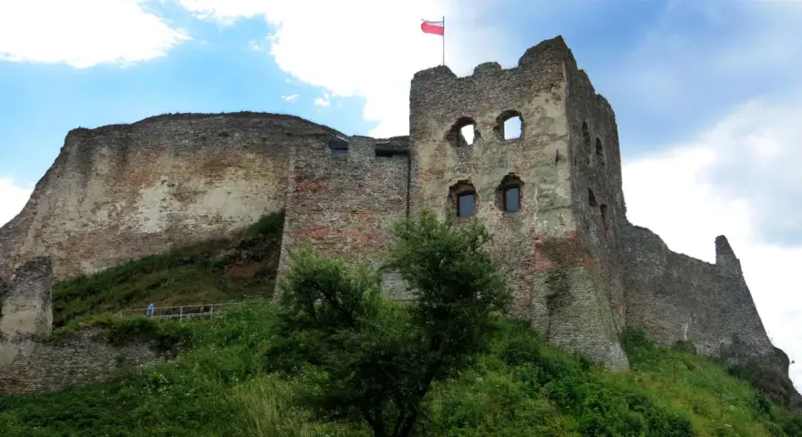 Ruiny zamku w Czorsztynie na wzgórzu, z polską flagą na wieży.