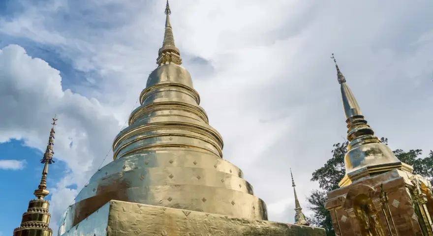 Złote stupy świątyni Wat Phra Singh w Chiang Mai na tle błękitnego nieba z chmurami.