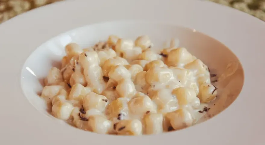 Kluski gnocchi w kremowym sosie z tartą truflą na białym talerzu.