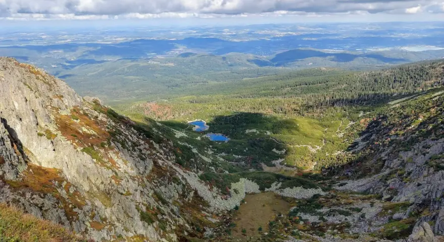Widok z góry na skaliste zbocze, dolinę z dwoma stawami i lasy w tle.