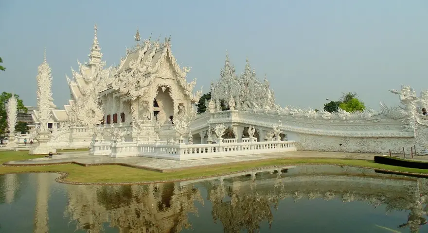 Biała świątynia Wat Rong Khun w Tajlandii z odbiciem w stawie.