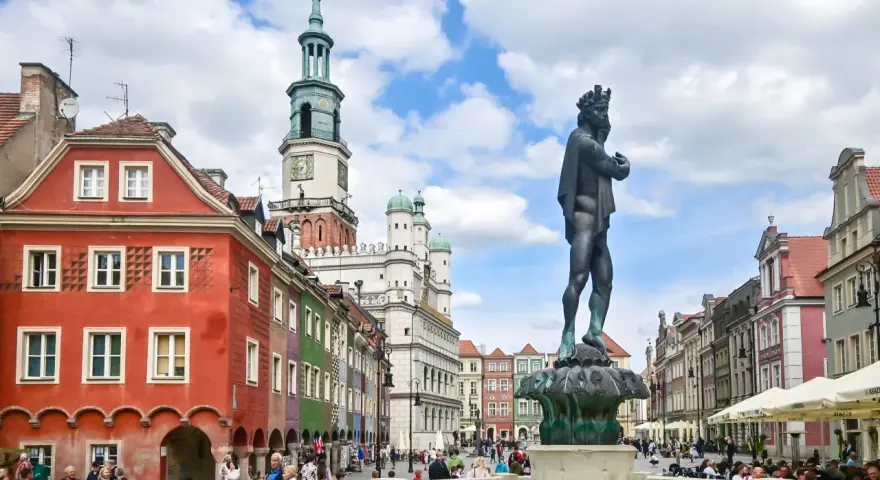 Pomnik króla na Rynku w Poznaniu, w tle kolorowe kamienice i ratusz.