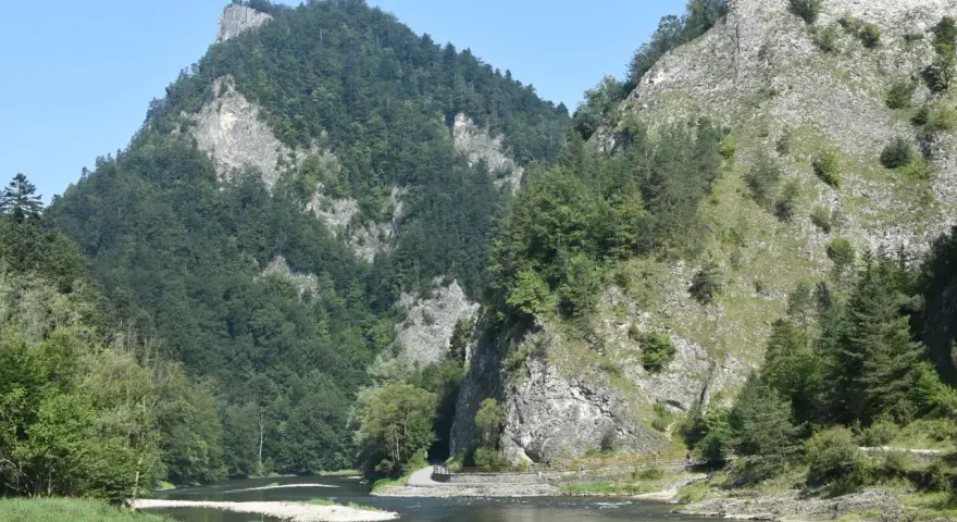 Rzeka Dunajec w przełomie, otoczona stromymi, zalesionymi górami i skalnymi zboczami.
