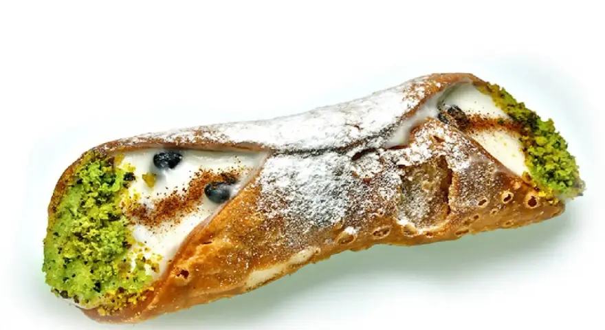 Sycylijski cannolo z kremem, pistacjami i borówkami, posypany cukrem pudrem.
