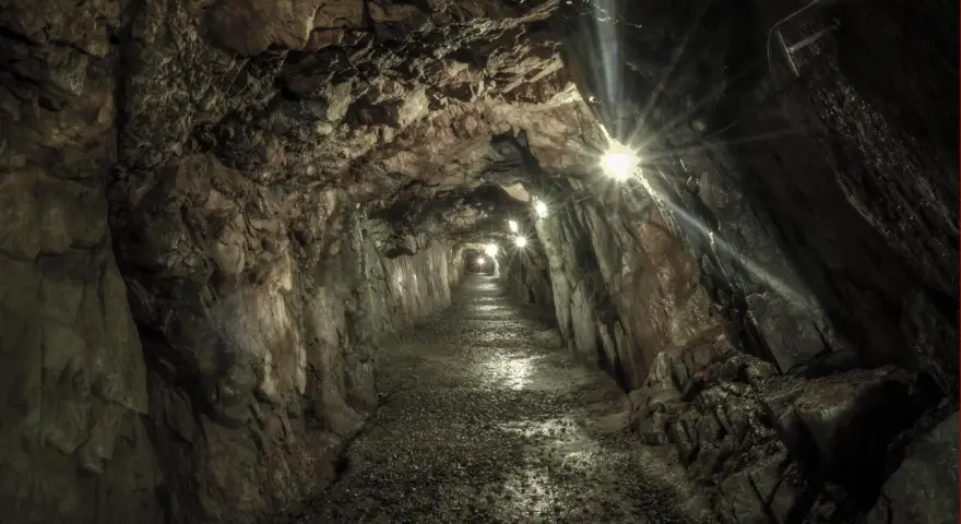 Wydrążony tunel skalny z oświetleniem, kamienista ścieżka.