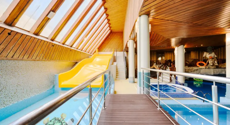 Wnętrze hotelowe z basenem, zjeżdżalnią i jacuzzi, drewniany sufit i ściany.