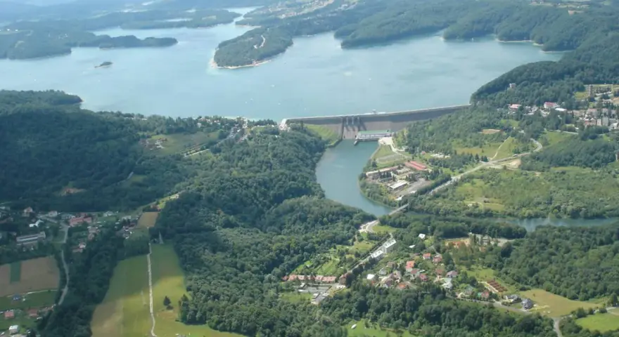 Widok z lotu ptaka na zalesione wzgórza, jezioro i zaporę wodną.