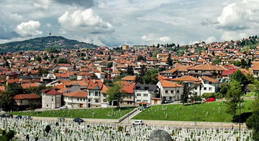 Widok na cmentarz i miasto z dachami z czerwonej dachówki pod zachmurzonym niebem.