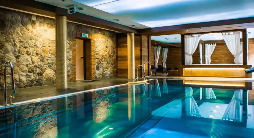 Basen w hotelu SPA z kamienną ścianą i drewnianymi elementami, z zasłonami w tle.