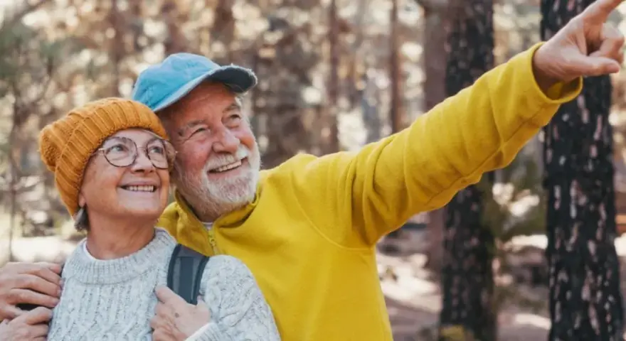 Uśmiechnięta para seniorów w górach, mężczyzna wskazuje palcem.