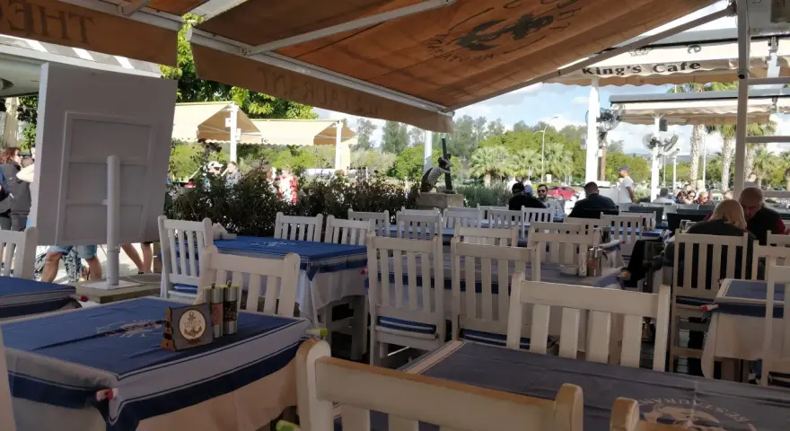 Stoliki w restauracji z niebiesko-białymi obrusami i białymi krzesłami, pod markizą.