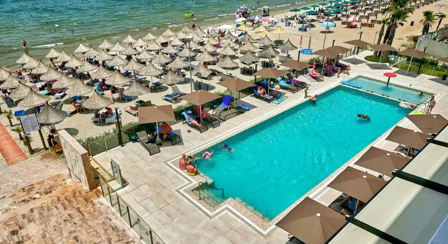 Widok z lotu ptaka na hotelowy basen i plażę z leżakami i parasolami w Durrës, Albania.