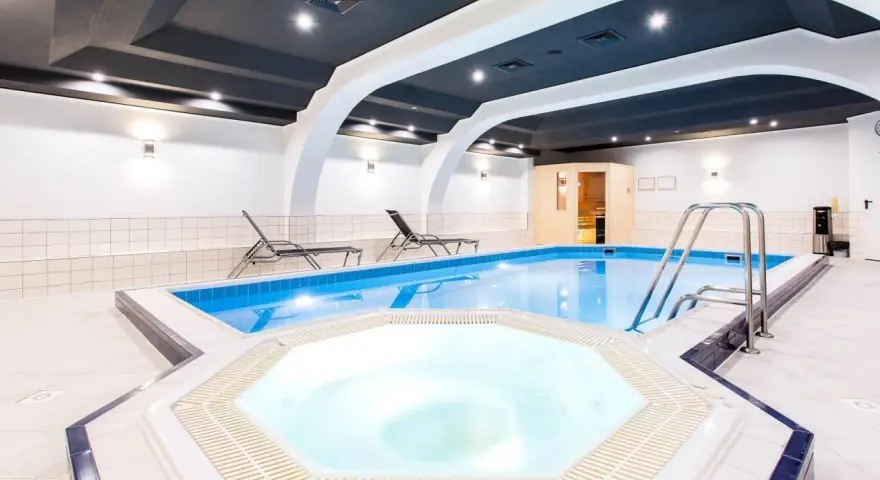 Wnętrze hotelowe z basenem, jacuzzi, sauną i leżakami.