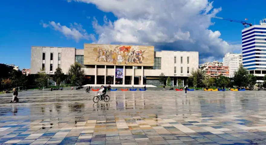 Plac w Tiranie z budynkiem Narodowego Muzeum Historii i kolorowymi pufami.