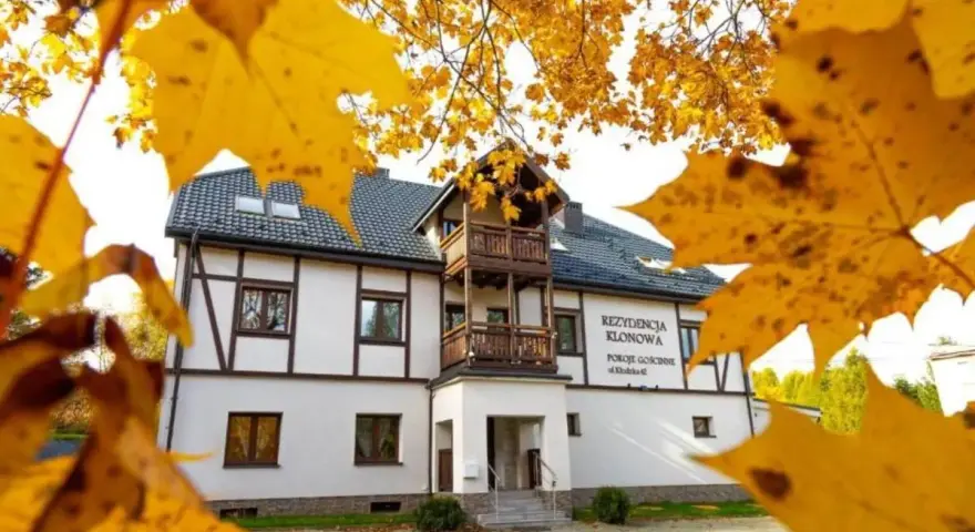 Dom z drewnianymi elementami i balkonem, otoczony jesiennymi liśćmi.