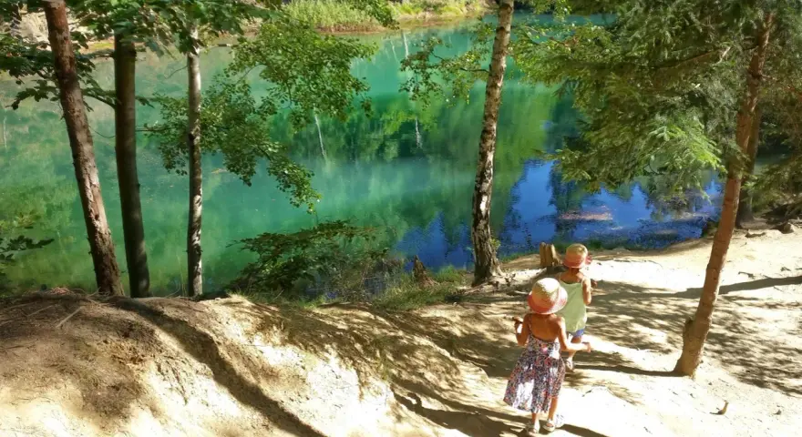 Dwie dziewczynki w słomkowych kapeluszach idą ścieżką nad turkusowym jeziorem.