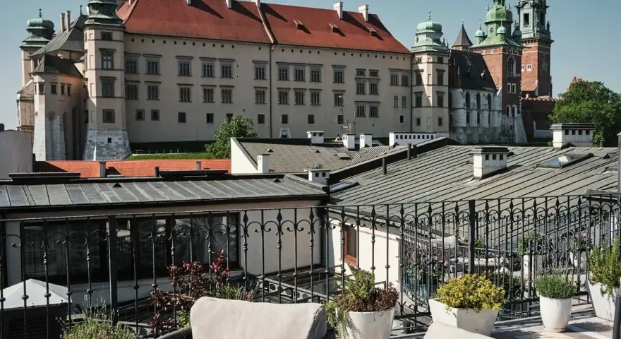 Widok z tarasu na Wawel, z meblami wypoczynkowymi i roślinami w donicach.