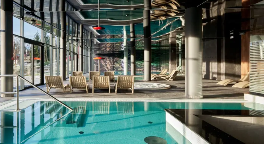 Basen z turkusową wodą i leżakami w nowoczesnym hotelowym spa.