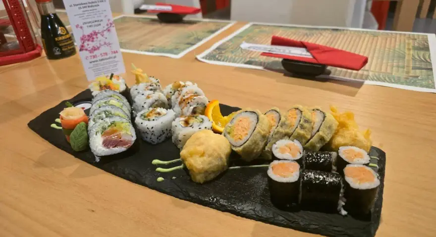 Talerz sushi z różnymi rolkami, w tym smażonymi i z łososiem, na czarnej desce.