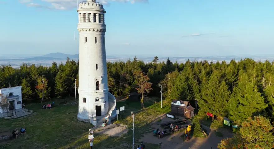 Kamienna wieża widokowa na szczycie góry otoczona lasem, z widokiem na krajobraz.