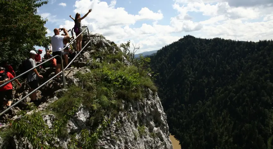 Grupa turystów na skalistym szczycie z widokiem na Pieniny i Dunajec.