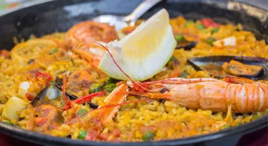 Paella z owocami morza i cytryną w czarnej patelni.