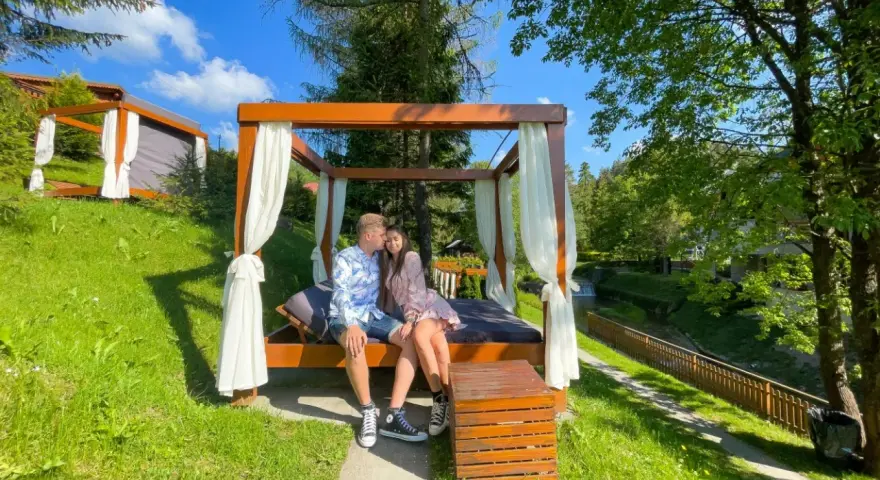Para siedząca na łóżku pod baldachimem w otoczeniu zieleni.