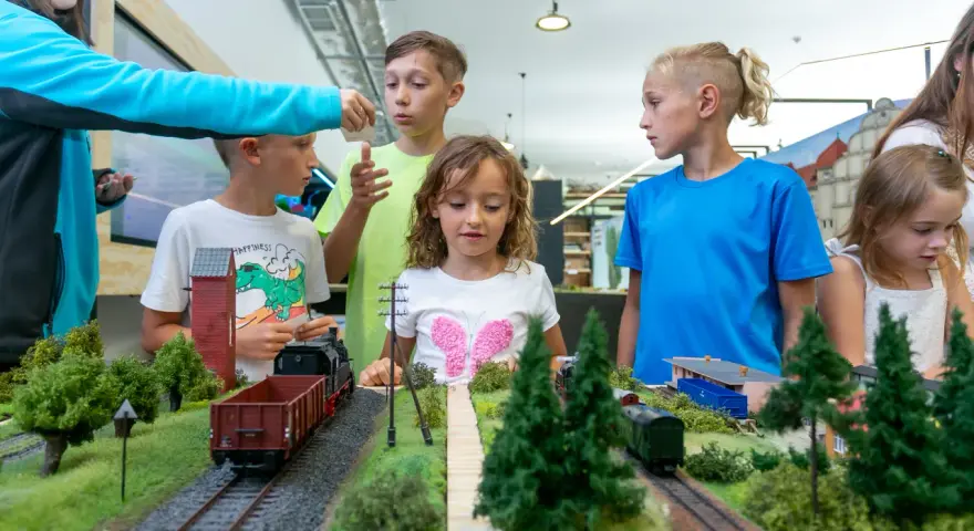 Dzieci oglądają makietę kolejową z pociągami i budynkami.