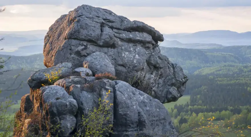 Skaliste formacje w Górach Stołowych z widokiem na zielone wzgórza i lasy.