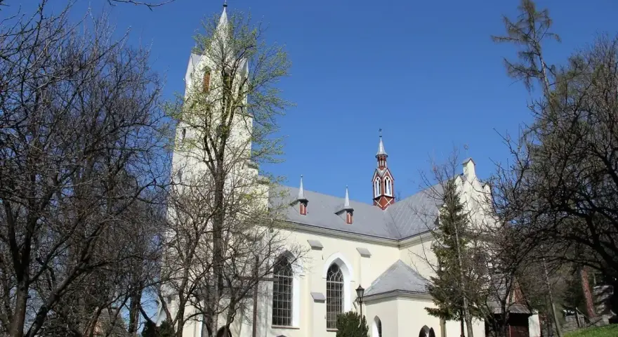 Jasny kościół św. Wojciecha w Szczawnicy z wieżą, otoczony drzewami.