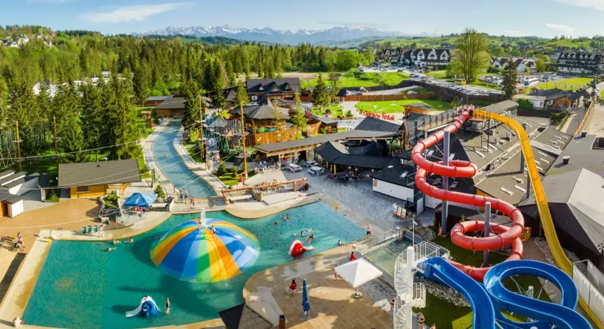 Widok z lotu ptaka na kompleks basenów i zjeżdżalni wodnych z górami w tle.